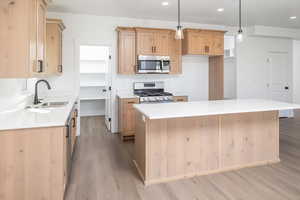 Kitchen with appliances with stainless steel finishes, hanging light fixtures, light wood-type flooring, light brown cabinets, and recessed lighting