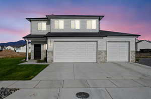 Traditional home featuring stone siding, driveway, a front lawn, and roof with shingles