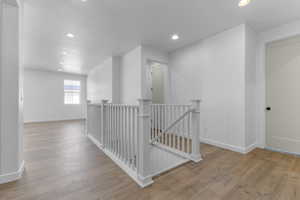 Hall with an upstairs landing, recessed lighting, light wood finished floors, and a textured ceiling
