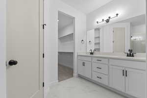 Full bathroom featuring double vanity, a spacious closet, and light marble finish flooring