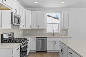 Kitchen with appliances with stainless steel finishes, white cabinets, decorative backsplash, and recessed lighting