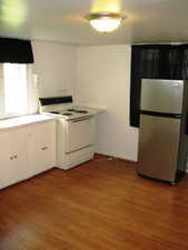 Kitchen with white range with electric cooktop, freestanding refrigerator, dark wood-style flooring, white cabinetry, and light countertops