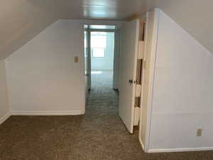 Additional living space featuring dark colored carpet and lofted ceiling