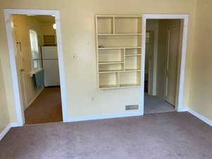 Unfurnished bedroom with carpet and freestanding refrigerator
