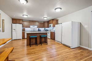 Kitchen featuring a textured ceiling, white appliances, light wood-type flooring, a center island, and a breakfast bar