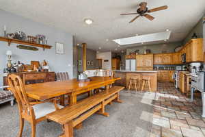 Dining area featuring a skylight, ceiling fan, a textured ceiling, light stone finish floors, and recessed lighting