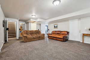 Carpeted living room with a textured ceiling and stairway
