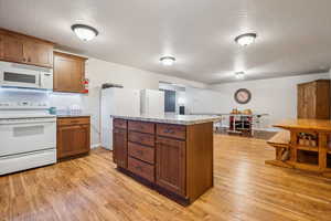 Kitchen with a textured ceiling, white appliances, brown cabinetry, light wood finished floors, and a center island