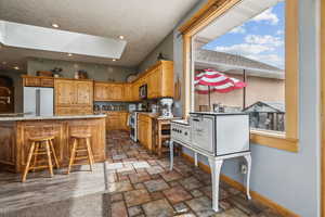 Kitchen featuring a skylight, a kitchen bar, appliances with stainless steel finishes, light stone finish flooring, and light stone countertops
