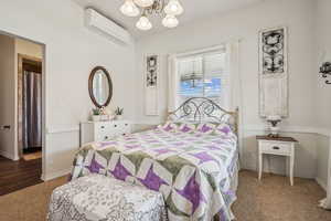 Carpeted bedroom featuring a wall mounted air conditioner and a chandelier