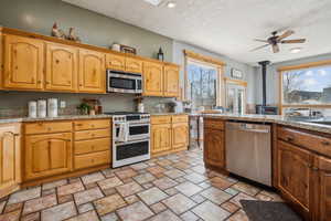 Kitchen featuring a textured ceiling, appliances with stainless steel finishes, light stone countertops, light stone finish floors, and ceiling fan