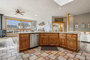 Kitchen featuring brown cabinetry, a wood stove, dishwasher, a textured ceiling, and stone tile flooring
