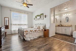 Bedroom with a textured ceiling, dark wood-type flooring, a ceiling fan, and ensuite bath