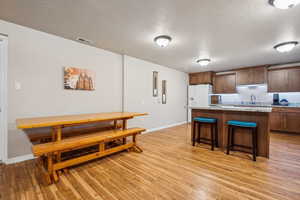 Kitchen featuring a textured ceiling, a breakfast bar, light wood finished floors, a center island, and white fridge with ice dispenser