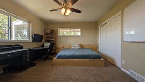 Carpeted bedroom featuring a closet, an office area, and a ceiling fan