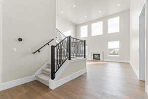 Staircase featuring a glass covered fireplace, wood-type flooring, recessed lighting, and a towering ceiling