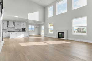Unfurnished living room with light wood-type flooring, a glass covered fireplace, a chandelier, a towering ceiling, and recessed lighting
