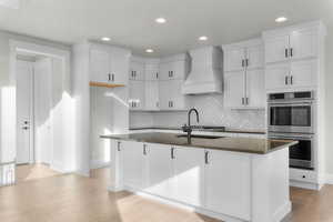 Kitchen with stainless steel double oven, recessed lighting, light wood-style flooring, white cabinetry, and dark stone counters