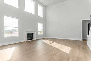 Unfurnished living room featuring a high ceiling, a glass covered fireplace, light wood finished floors, and recessed lighting