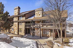 Snow covered house with a chimney, stone siding, a balcony, and a patio