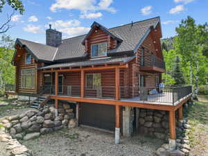 Rear view of house with log siding, a chimney, a shingled roof, stairs, and a porch
