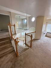 Stairs with a chandelier, carpet, plenty of natural light, and a textured ceiling