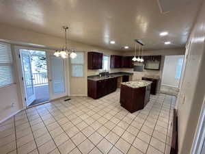 Kitchen featuring a chandelier, hanging light fixtures, light tile patterned flooring, a textured ceiling, and dark stone countertops