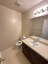 Half bathroom with a textured ceiling, vanity, and light floors