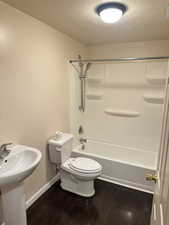 Full bathroom with a textured ceiling, shower / washtub combination, and dark wood-type flooring