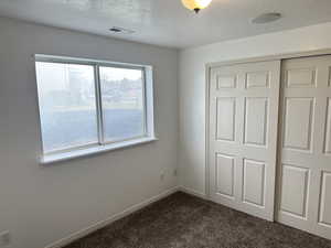 Unfurnished bedroom featuring dark colored carpet, a textured ceiling, and a closet