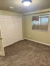 Unfurnished bedroom with dark carpet, a textured ceiling, and a closet