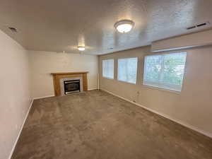Unfurnished living room with healthy amount of natural light, a tiled fireplace, a textured ceiling, and carpet flooring