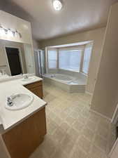 Full bath with vanity, a shower stall, a bath, and a textured ceiling