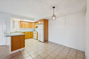 Kitchen with white appliances, a peninsula, light countertops, decorative light fixtures, and light tile patterned flooring