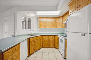 Kitchen featuring white appliances, light tile patterned flooring, light countertops, brown cabinetry, and a peninsula