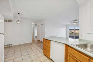 Kitchen with white appliances, light countertops, hanging light fixtures, a peninsula, and light tile patterned floors