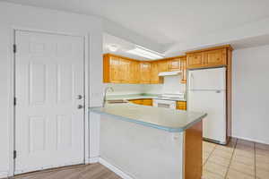 Kitchen with white appliances, a peninsula, light countertops, light tile patterned floors, and under cabinet range hood