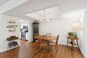 Dining room featuring a raised ceiling, dark wood-type flooring, a chandelier, and crown molding