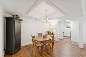 Dining area featuring a tray ceiling, wood finished floors, ornamental molding, and a chandelier