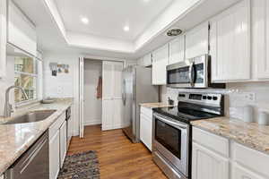 Kitchen with appliances with stainless steel finishes, dark wood finished floors, white cabinets, light stone countertops, and a raised ceiling