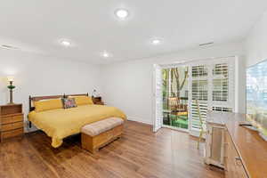 Bedroom with multiple windows, dark wood finished floors, access to outside, and recessed lighting