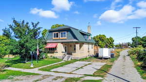 View of front facade featuring a chimney, a gambrel roof, a porch, a front lawn, and brick siding