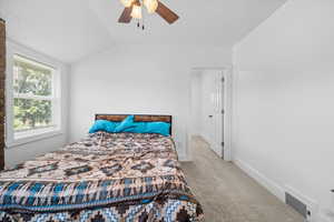 Carpeted bedroom featuring vaulted ceiling and a ceiling fan