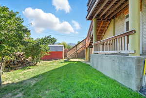 View of grassy backyard featuring stairs and a storage shed