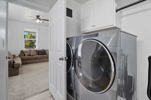 Bathroom/Laundry area featuring a ceiling fan, light colored carpet, cabinet space, and washing machine and clothes dryer