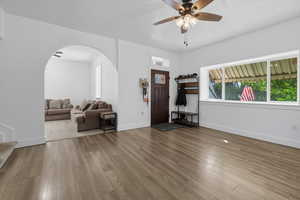 Living room featuring light wood-style flooring, a ceiling fan, arched walkways, and a textured ceiling