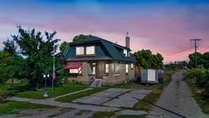 View of front facade featuring a chimney, brick siding, a front lawn, and a gambrel roof