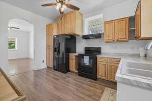 Kitchen featuring a ceiling fan, black appliances, light countertops, light wood-style flooring, and arched walkways