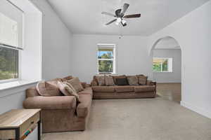 Carpeted living area with arched walkways, a textured ceiling, and a ceiling fan
