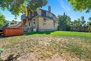 Back of house featuring a hot tub, a chimney, brick siding, mansard roof, and stairs